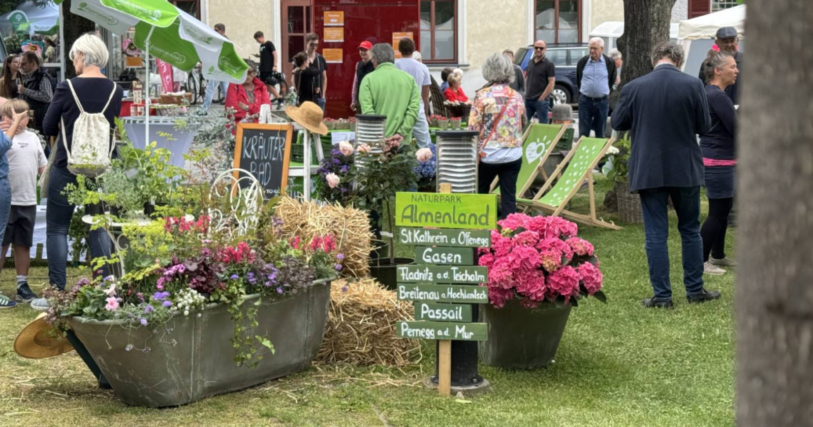 Ein Gartenfest mit vielen Menschen, Blumen und Pflanzenständen. Dekorationen wie Heuballen, Schilder und Liegestühle sorgen für eine gemütliche Atmosphäre | Credit: Christian Strassegger