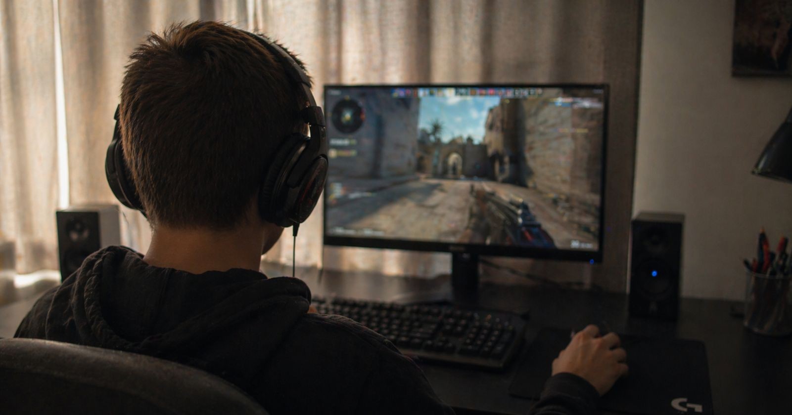 Jugendlicher mit Kopfhörern spielt Videospiel am PC, während ein Amoklauf an einer Schule im Chat angekündigt wurde