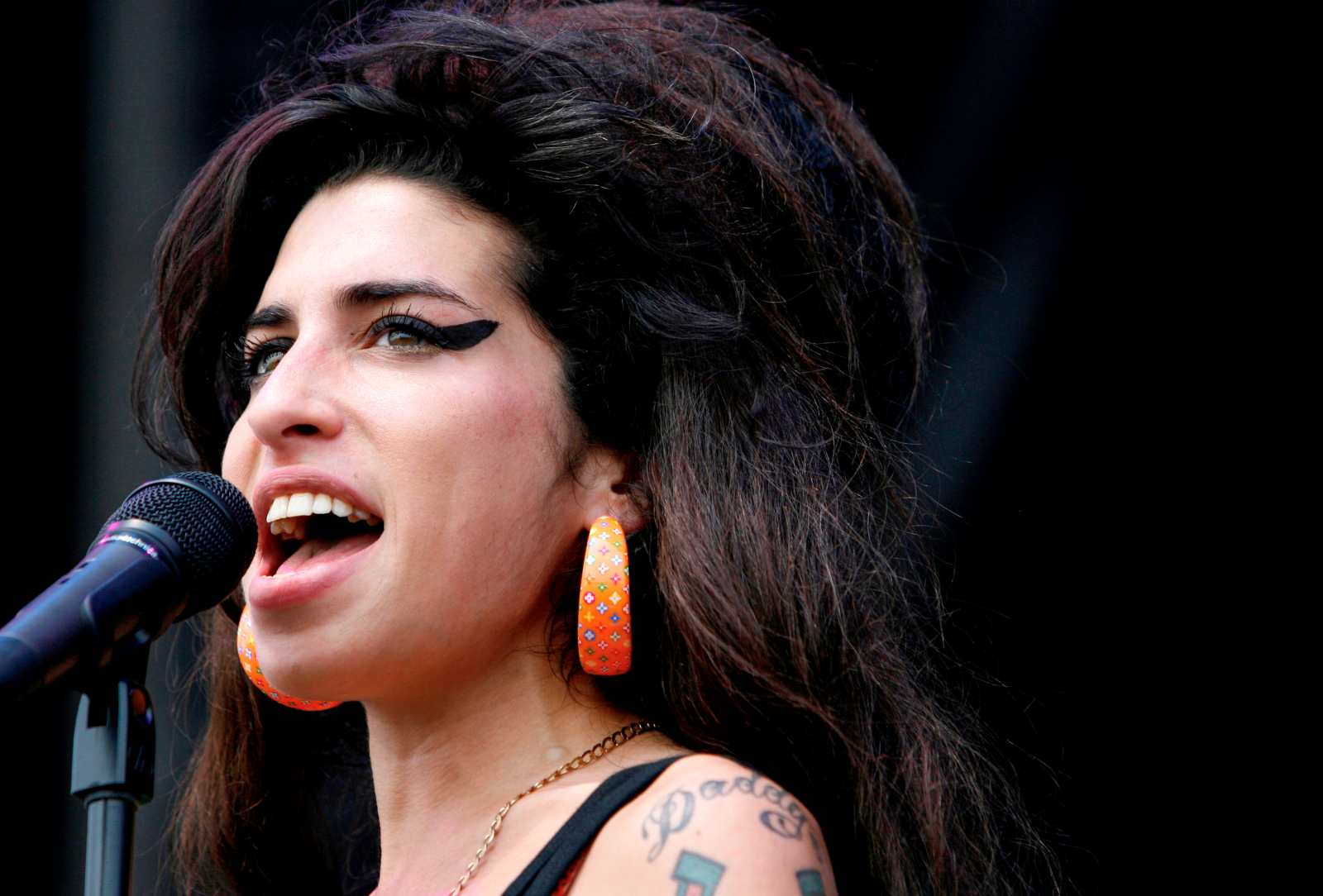 Sängerin Amy Winehouse mit markantem Lidstrich und großer Frisur singt ins Mikrofon auf der Bühne