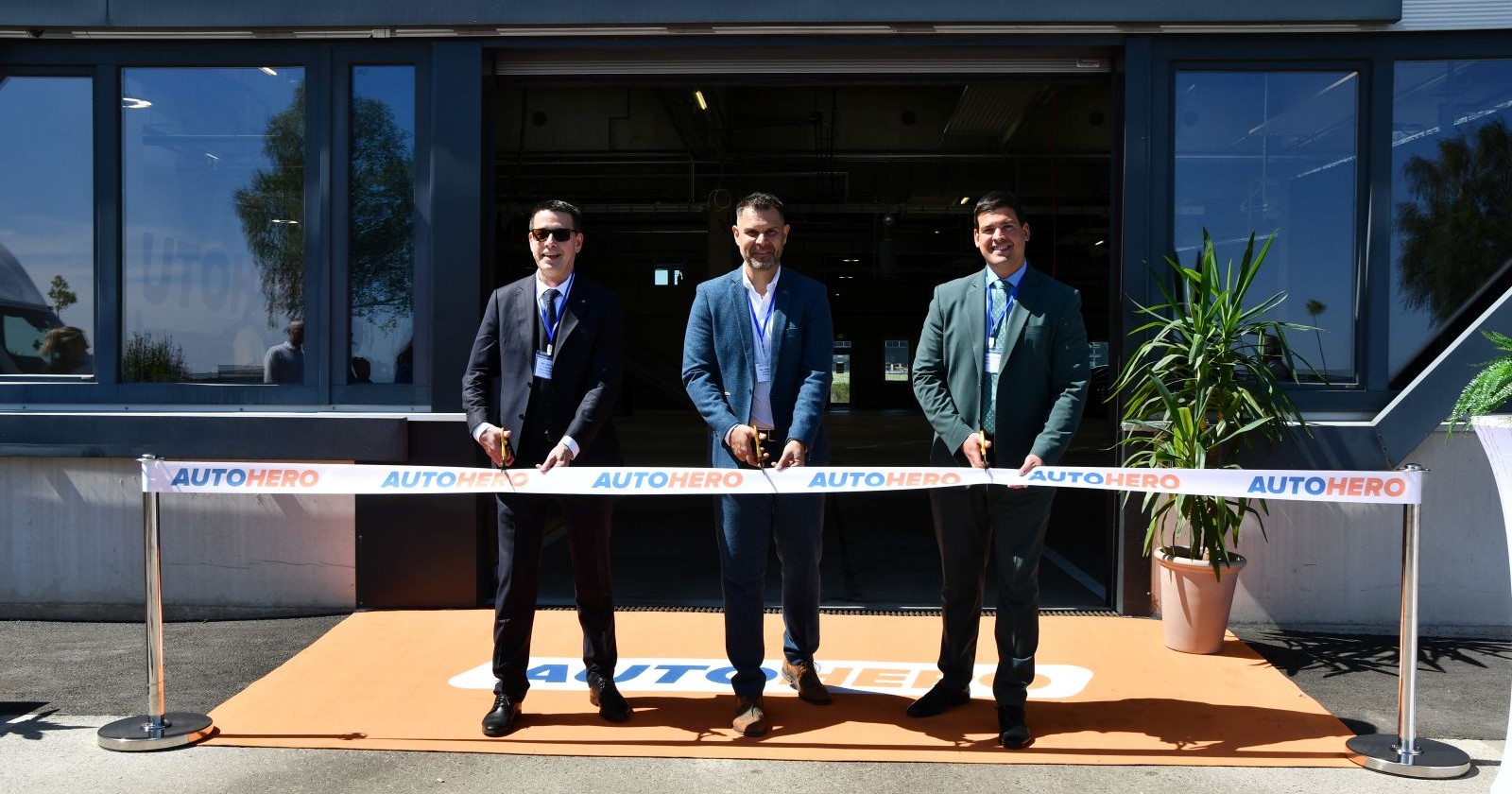 Drei Herren durchschneiden das rote Band vor dem neuen Firmengebäude