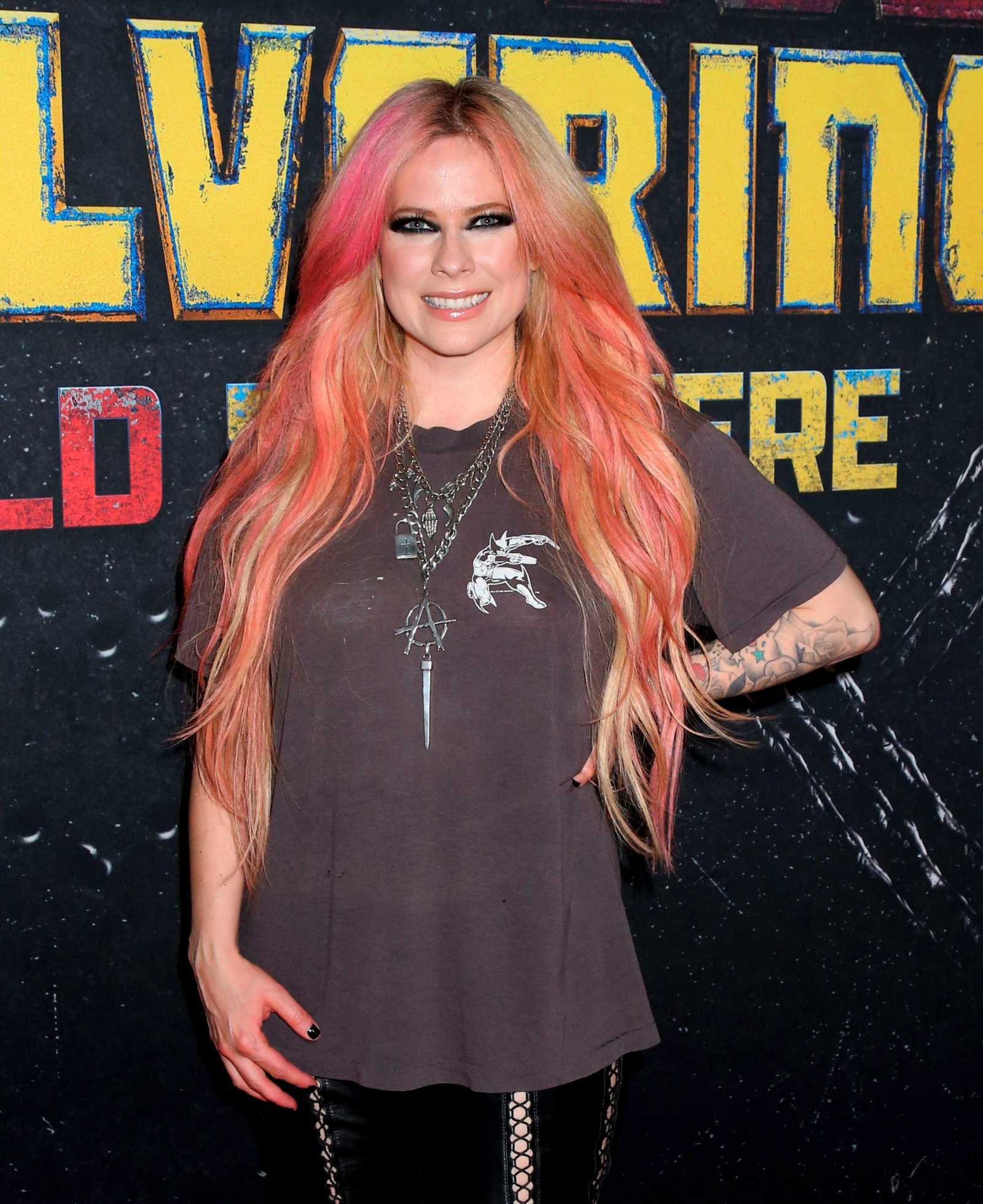 Avril Lavigne mit langen pink-blonden Haaren bei einem Event vor Fotowand