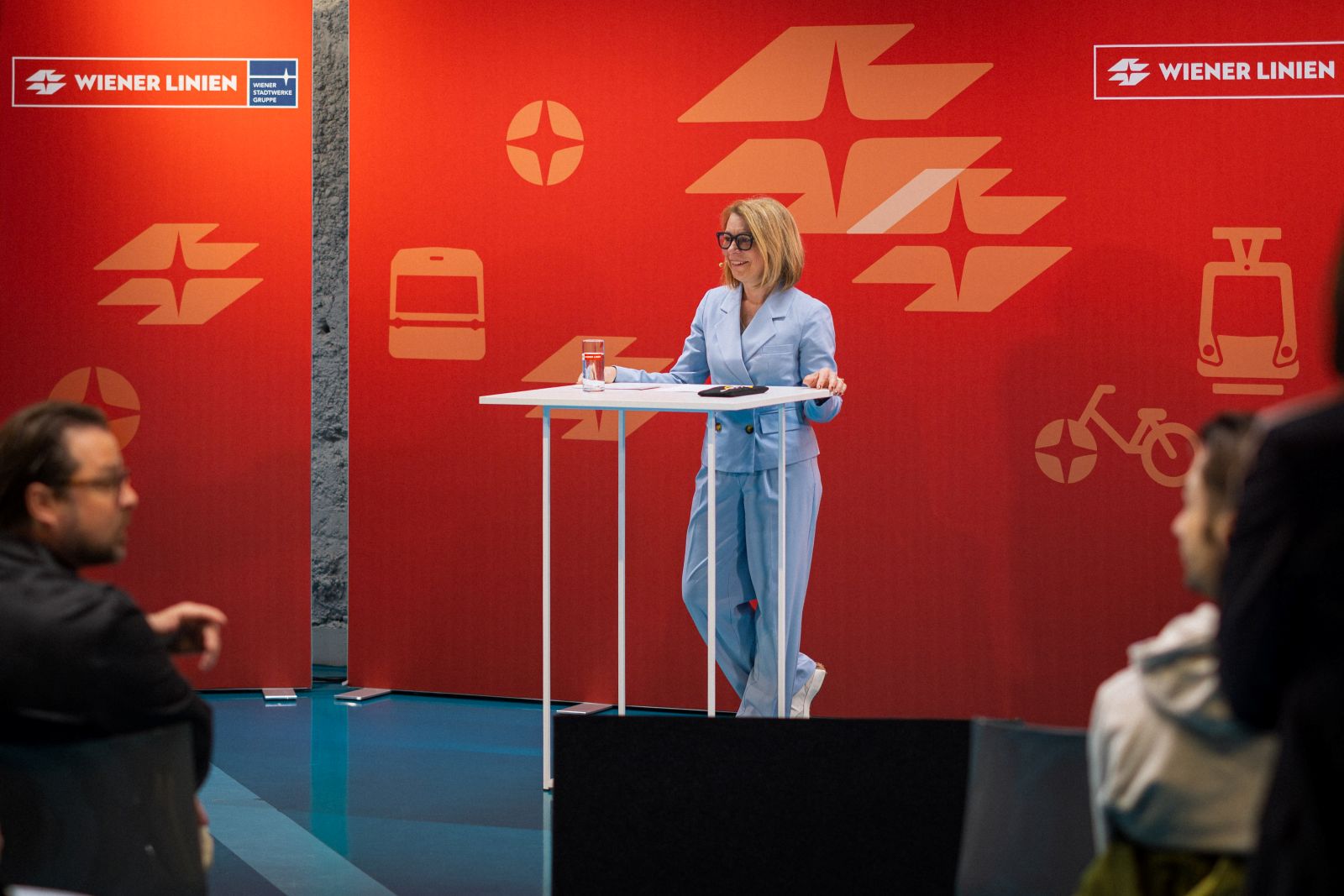 Wiener-Linien-Geschäftsführerin im hellblauen Hosenanzug vor einer roten Wand