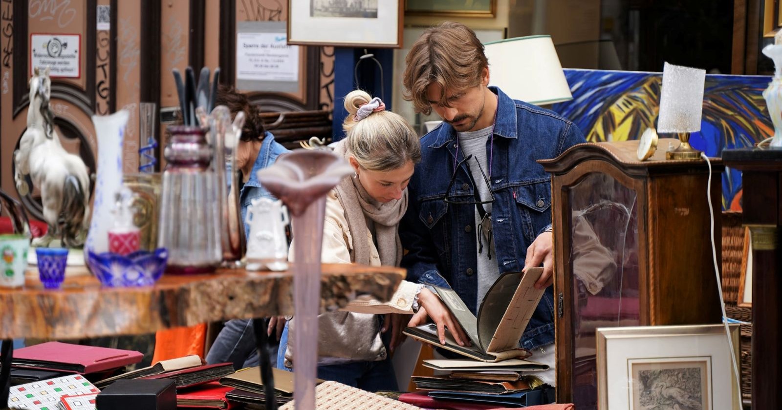 Besucher stöbern beim Flohmarkt Neubaugasse in Wien durch Vintage-Bücher, Bilderrahmen und Antiquitäten an einem Marktstand