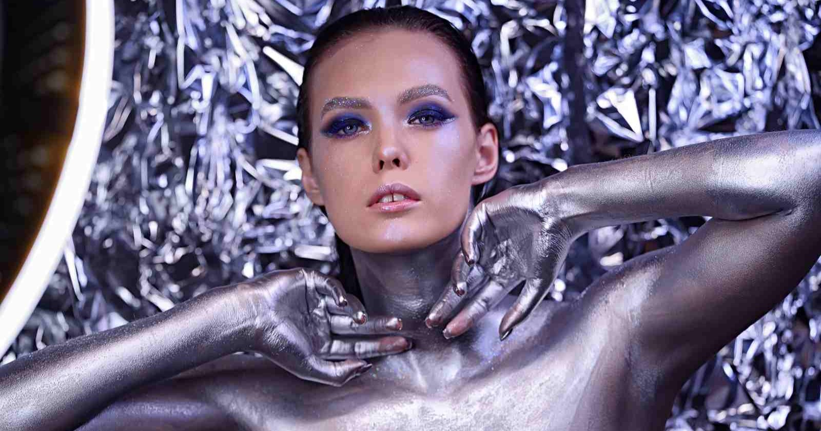 Frau mit silbernem Bodypainting und futuristischem Make-up vor glänzendem Hintergrund – Symbol für moderne Hightech-Beauty