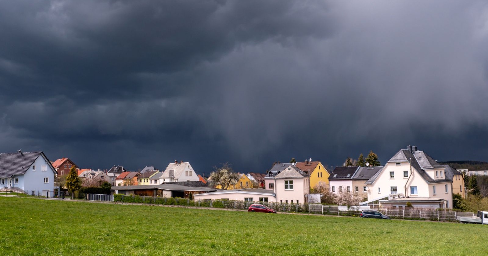 Gewitter am Ostersonntag: Dunkle Gewitterwolken über einem österreichischen Dorf mit Blick über eine saftig grüne Wiese im Frühling