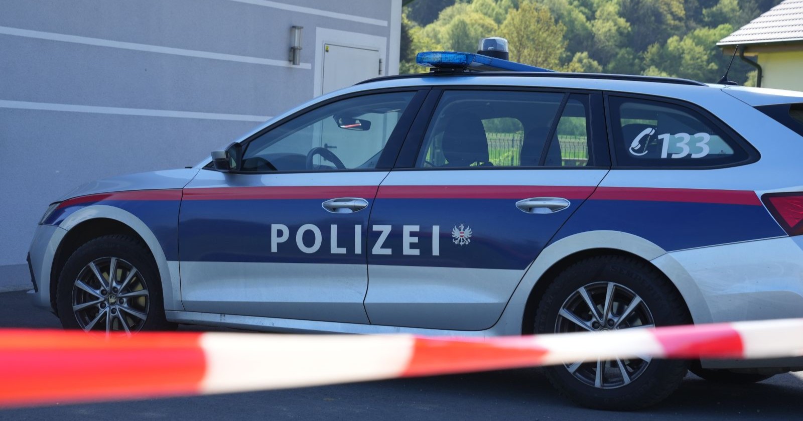 Ein Polizeiauto steht vor einem Haus, davor ist eine Absperrung