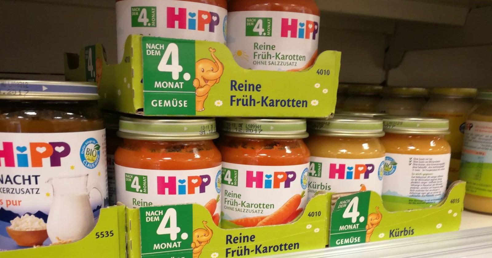 Mehrere Gläser HiPP-Babynahrung der Sorte Karotte und Kürbis stehen dicht gereiht in einem Supermarktregal, während Ermittlungen wegen möglicher Manipulation und Erpressung laufen.