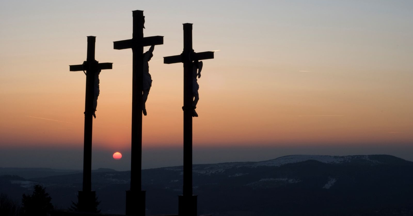 Kreuzigung Jesu auf Golgotha mit drei Kreuzen bei Sonnenuntergang; Themenbild für Karfreitag Bedeutung, Rituale und Traditionen.