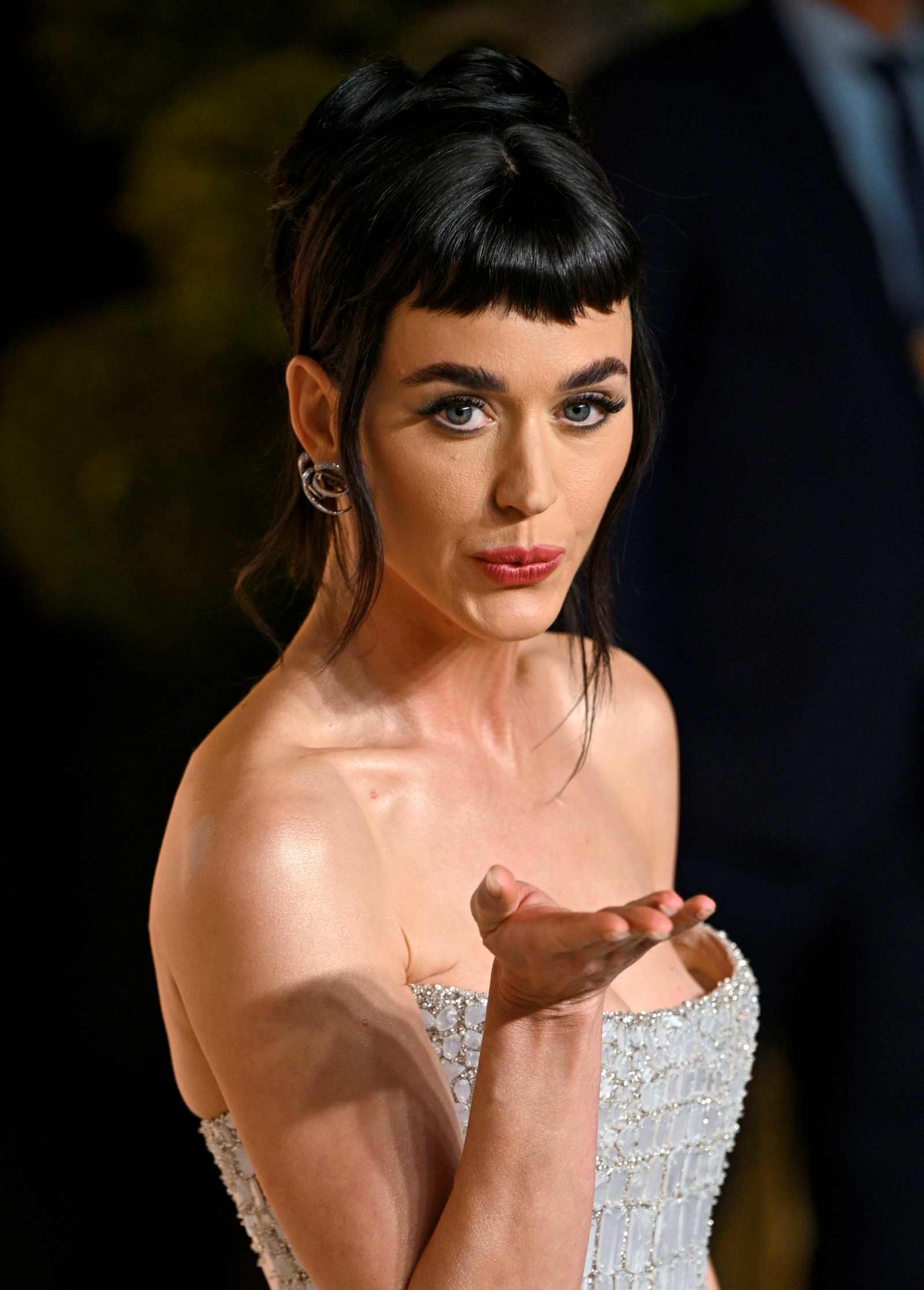 Katy Perry im eleganten trägerlosen Kleid bei einem Event, sie wirft eine Handkuss-Geste