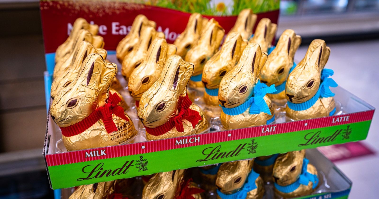 Mehrere Lindt Goldhasen stehen dicht nebeneinander in einem Supermarktregal und zeigen die typische goldene Verpackung mit Schleife.