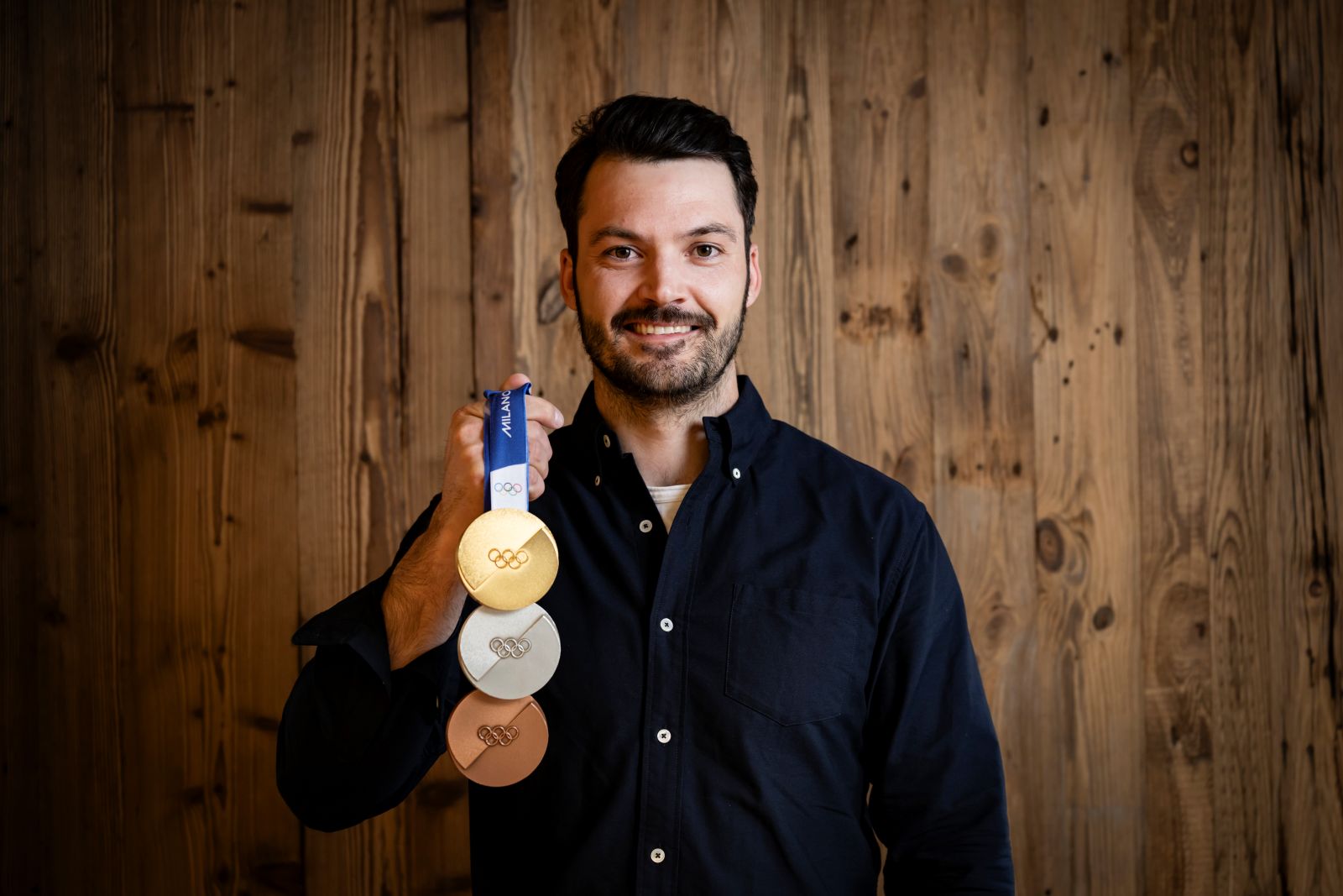 Ein dunkelhaariger Mann hält Olympia-Medaillen in die Kamera