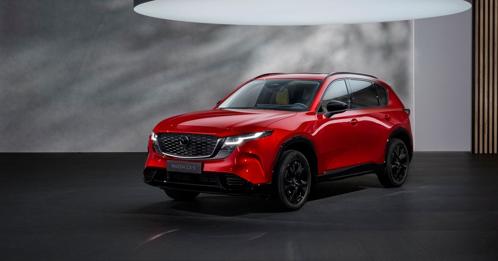 Eine roter Mazda CX 5 steht einem grau-schwarzen Raum. Über dem Auto ist ein sehr großes Licht zu sehen, das das Auto beleuchtet.