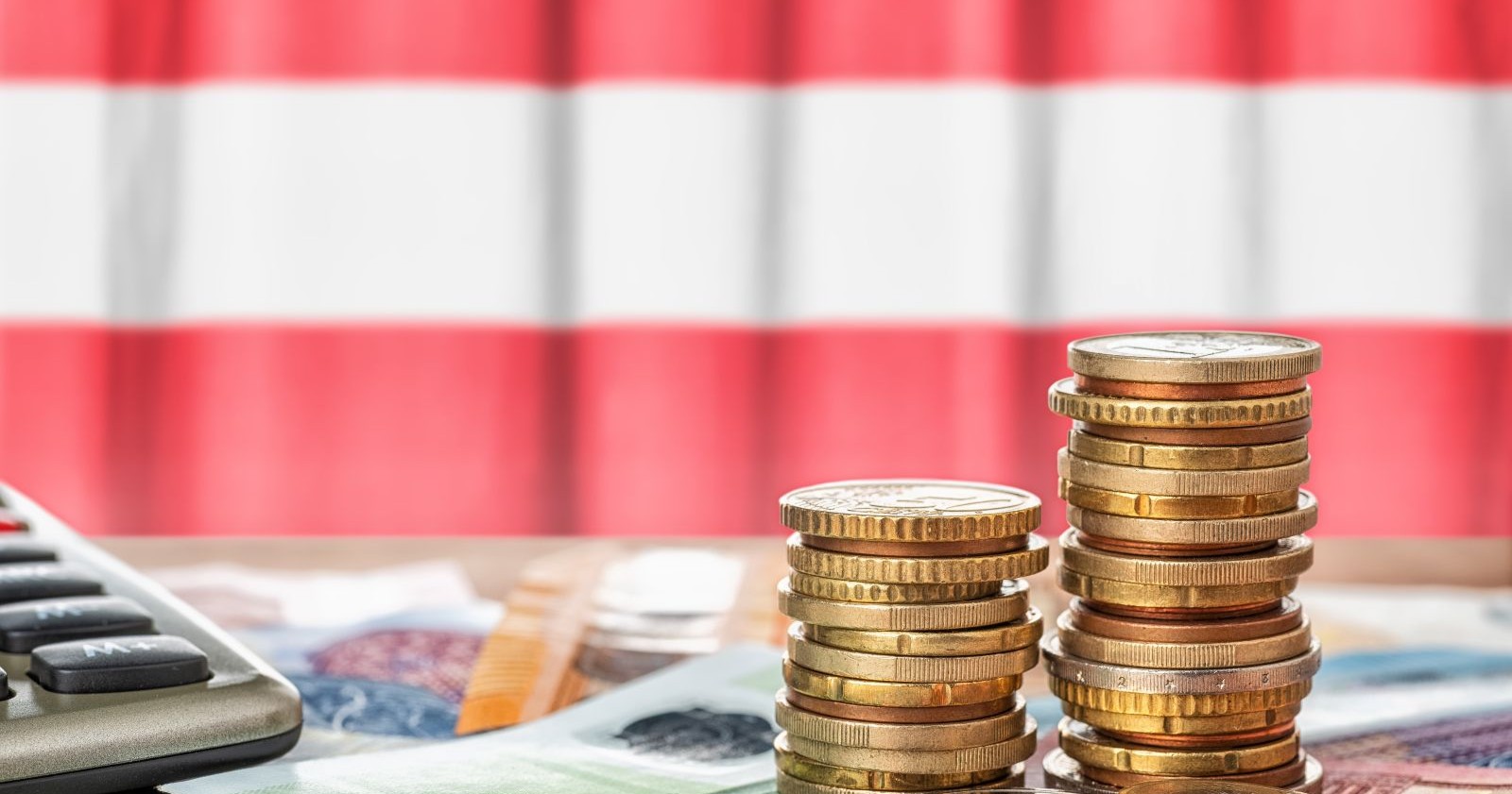 Euro-Münzen und Geldscheine mit Taschenrechner vor Österreich-Flagge symbolisieren Budget Österreich, Sparpaket, Steuern und Pensionen