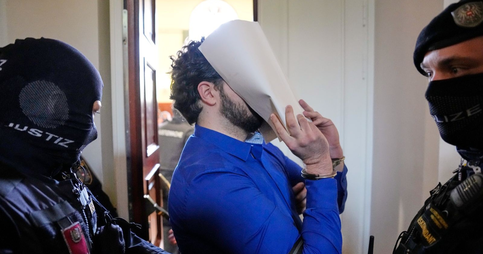Angeklagter im Terror-Prozess Wien wird von bewaffneten Justizbeamten abgeführt und verdeckt sein Gesicht im Gericht