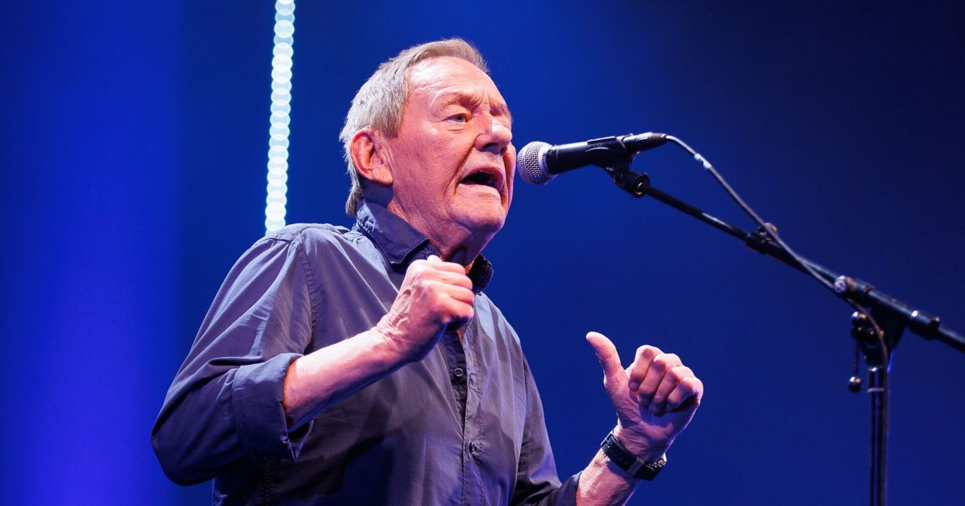 Wolfgang Ambros singt live auf der Bühne mit Mikrofon während eines Konzerts
