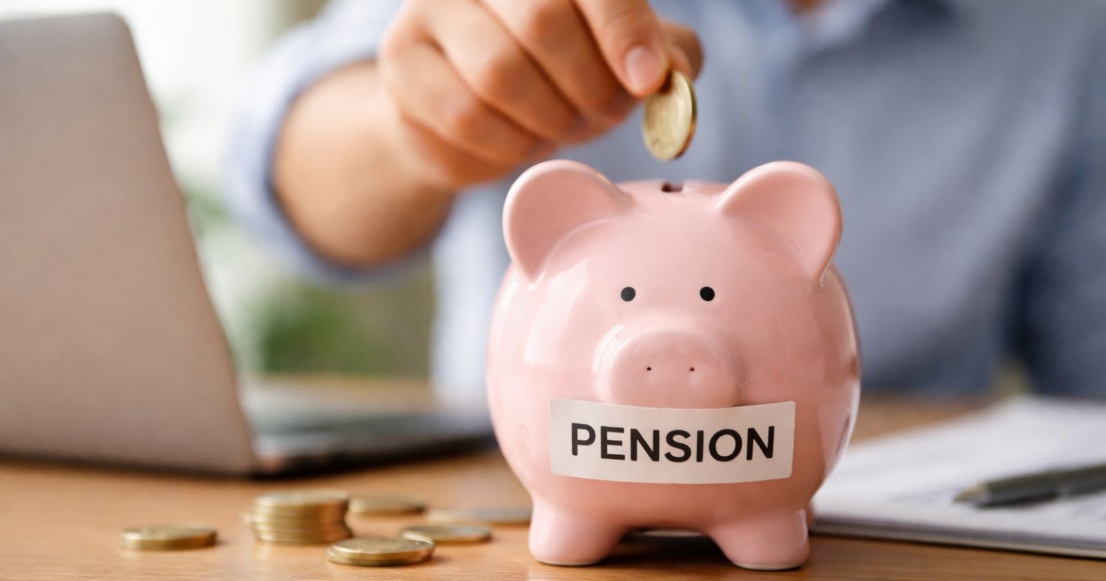 Symbolbild für Zusatzpension in Österreich: Eine Person legt Geld in ein Sparschwein, während sie ihre Altersvorsorge am Laptop organisiert.