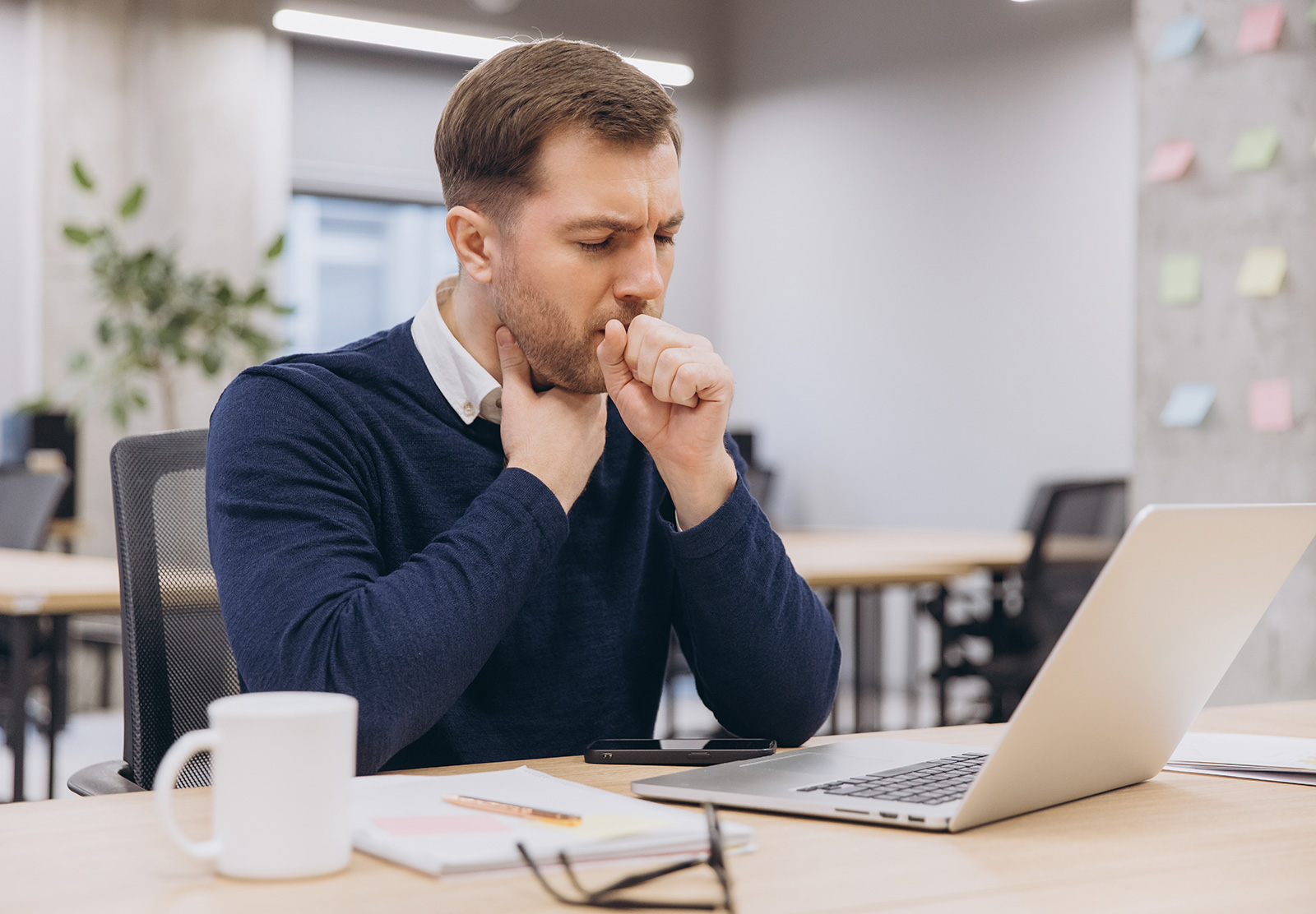 Mann räuspert sich bei der Arbeit am Laptop im Office | Credit: Anatoliy Cherkas/Shutterstock