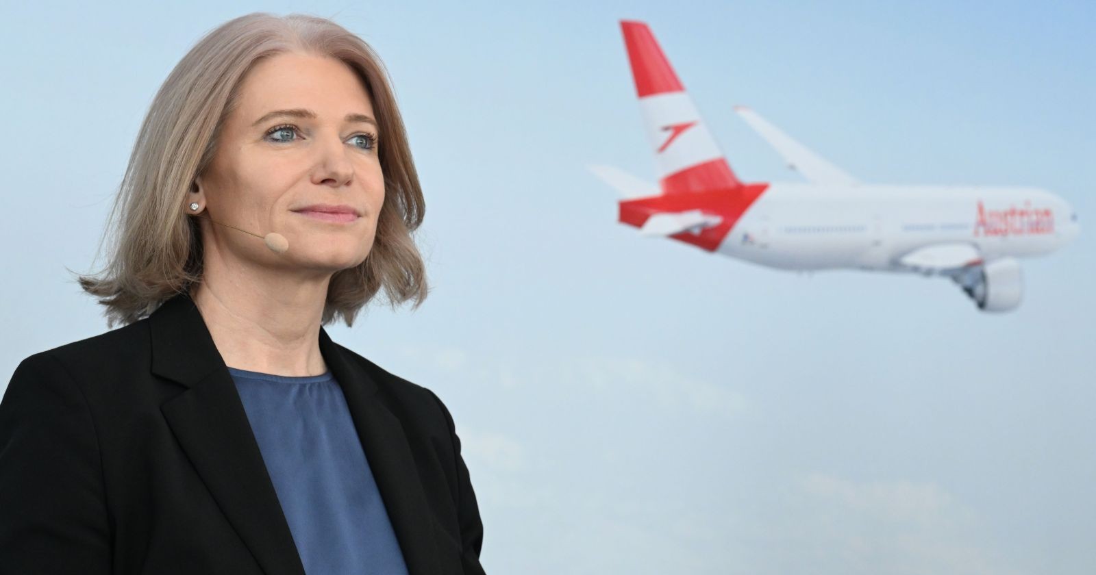 Frau spricht auf einer Pressekonferenz, dahinter ist ein Flieger zu sehen