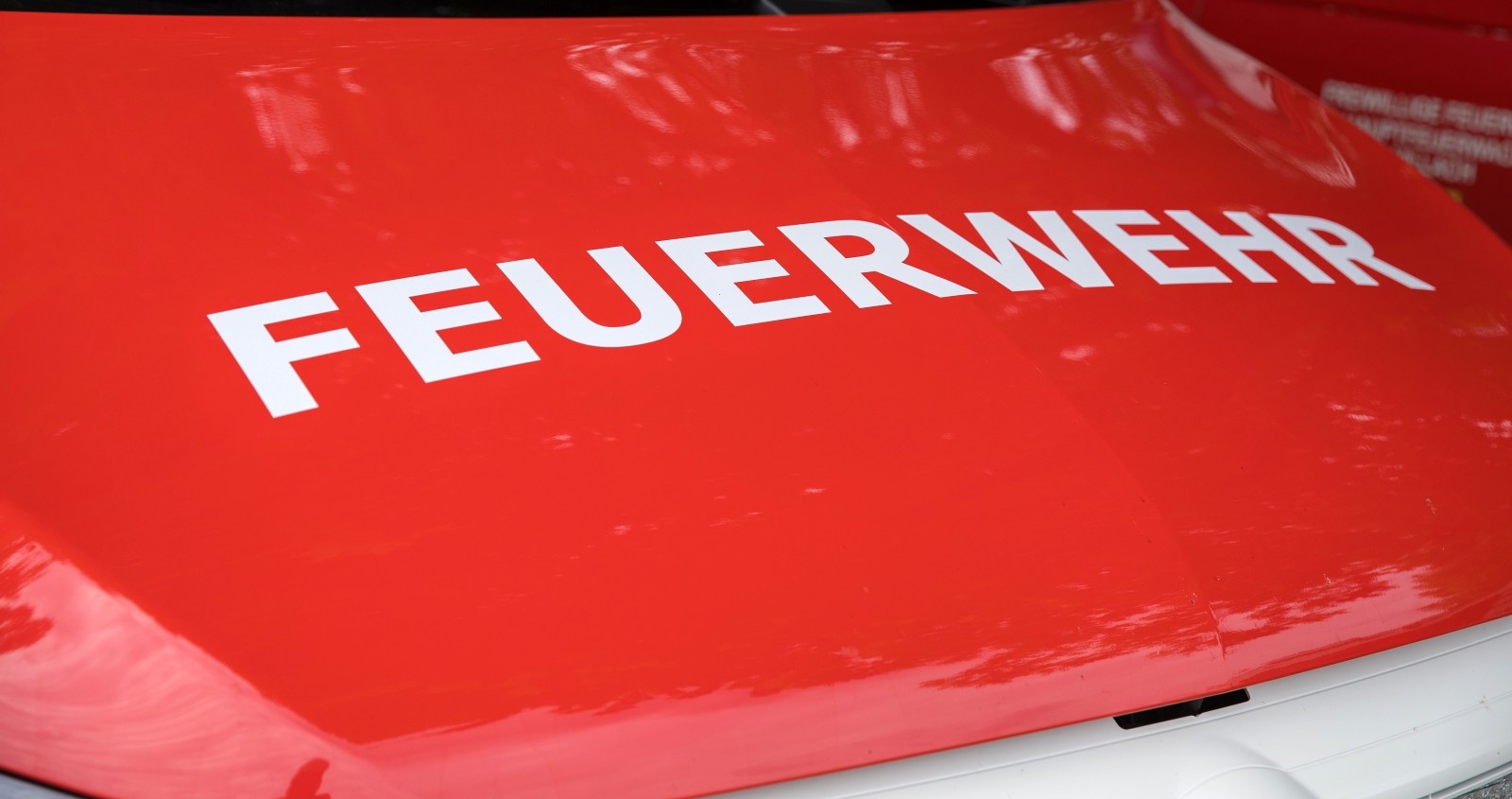 Nahaufnahme einer roten Feuerwehrlasterhaube mit 'FEUERWEHR'-Text, die das Design von Notfallfahrzeugen und die städtische Umgebung hervorhebt.