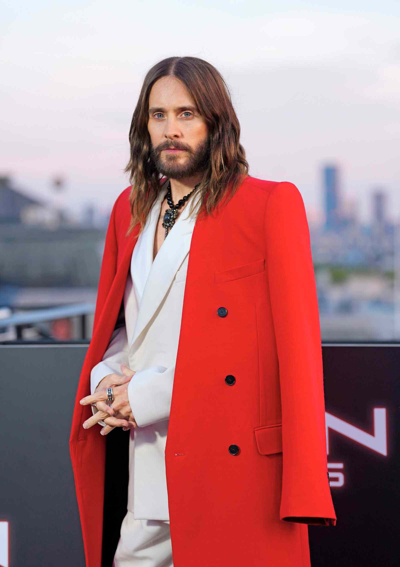 Jared Leto mit langen Haaren und Bart in rotem Mantel bei einem aktuellen Event.