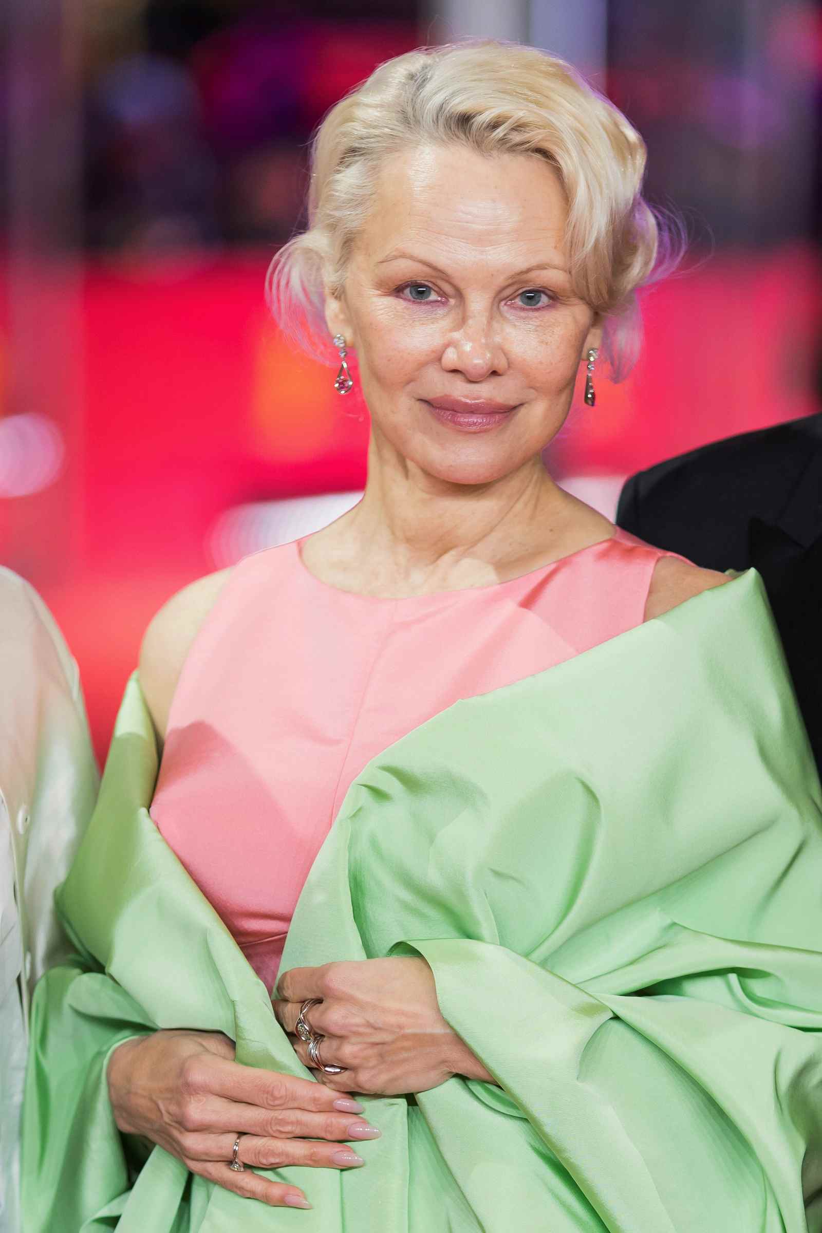 Pamela Anderson mit kurzer blonder Frisur und elegantem Pastell-Look bei einem aktuellen Event.
