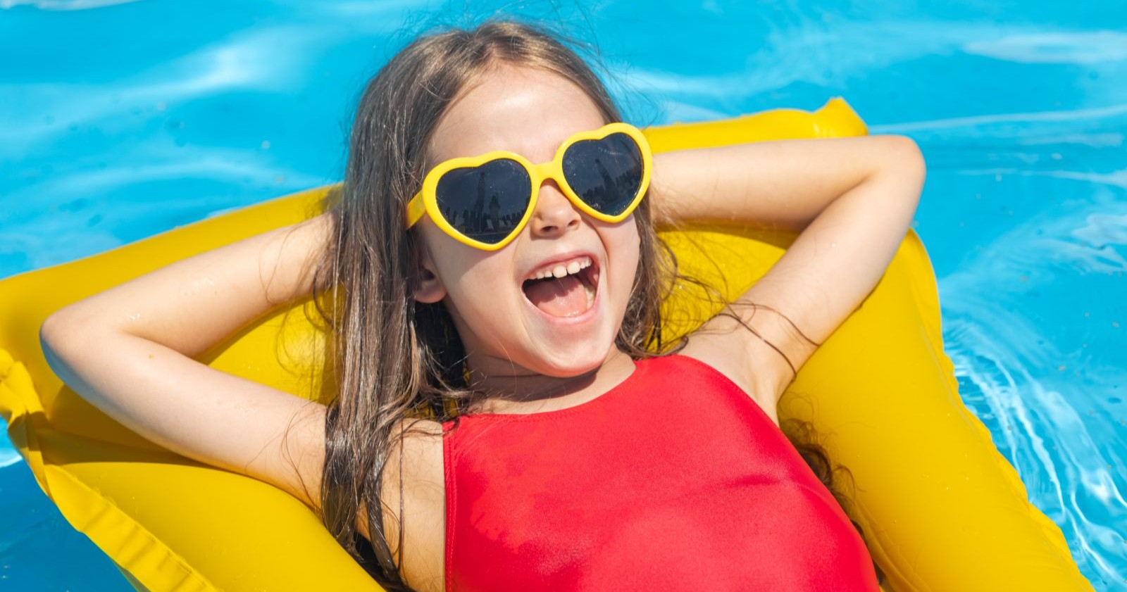 Ein Mädchen liegt in einem Pool auf einer gelben Luftmatratze.
