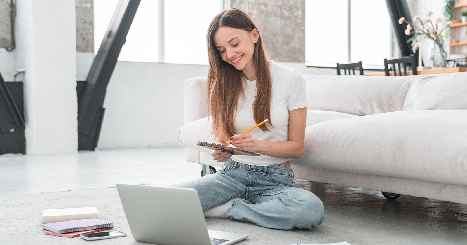 Frau sitzt am Boden ihres Eigenheims und macht sich Notizen vor ihrem Laptop | Credit: Inside Creative House/Shutterstock