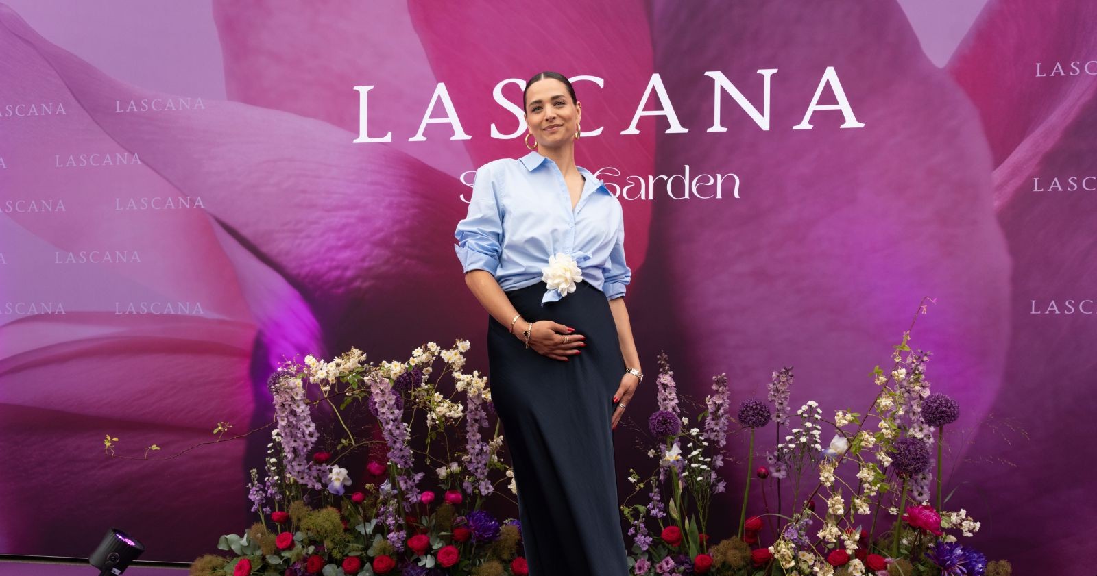 Amira Aly steht lächelnd und mit rundem Babybauch auf einem violetten Teppich auf der Lascana-Gala in Hamburg