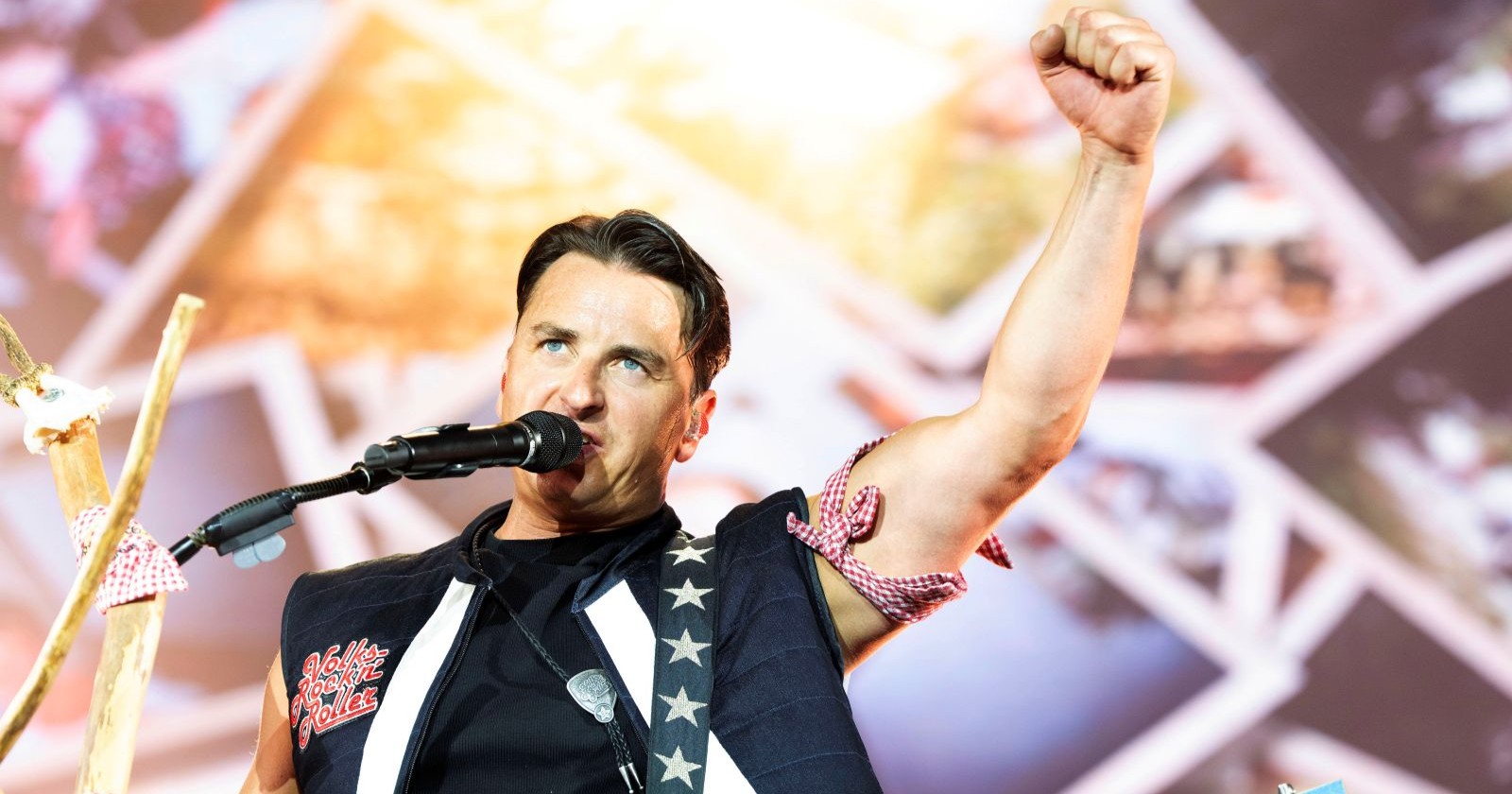 Andreas Gabalier bei einem Live-Auftritt auf der Bühne. Der Volks-Rock’n’Roller singt ins Mikrofon und jubelt mit erhobener Faust vor seinem Publikum.