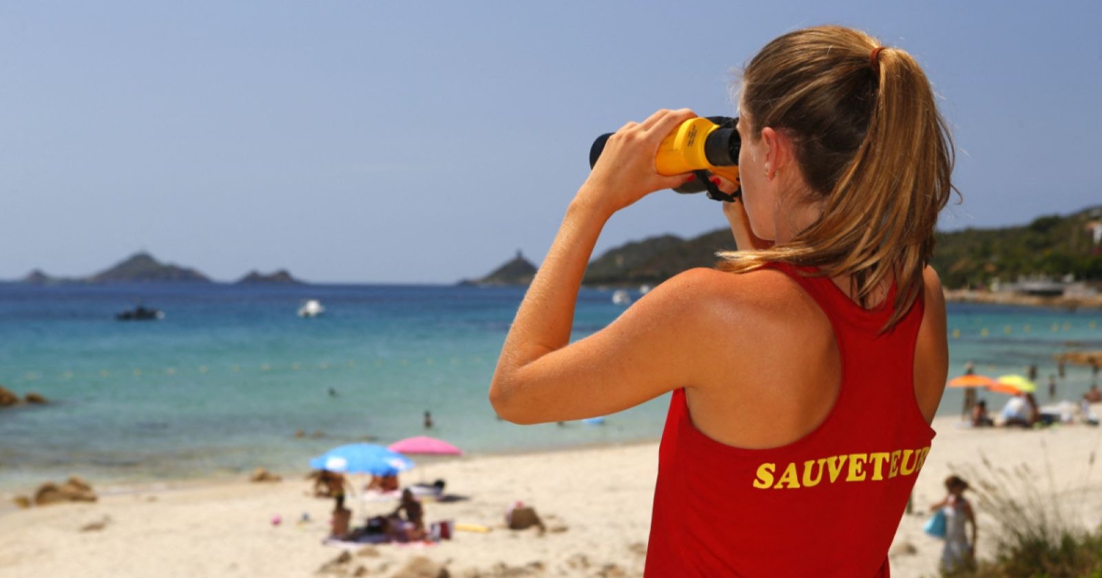 Bademeisterin in rotem Shirt sieht aufs Meer mit einem Fernglas