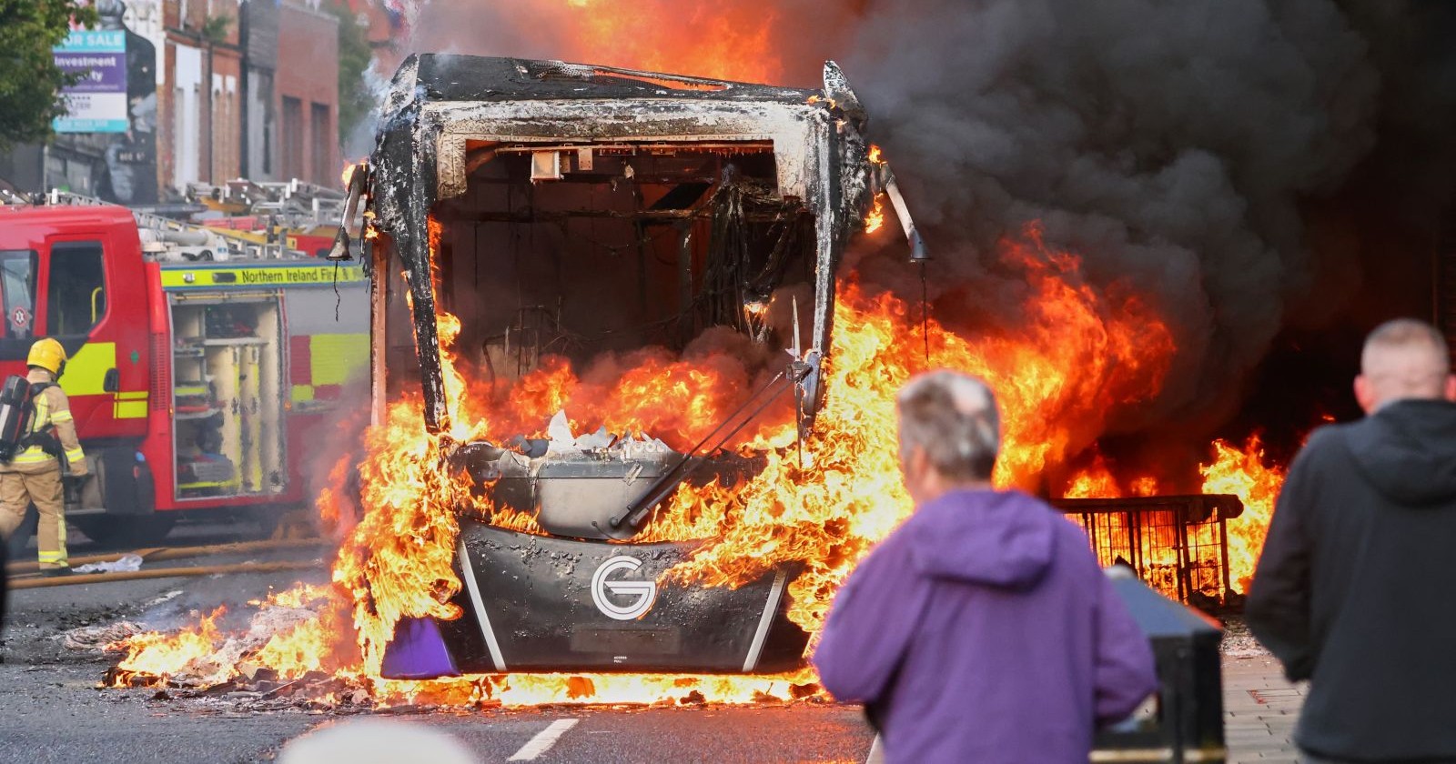 Brennender Bus bei Ausschreitungen in Belfast, Feuerwehr im Einsatz, Flammen und schwarzer Rauch auf Straße