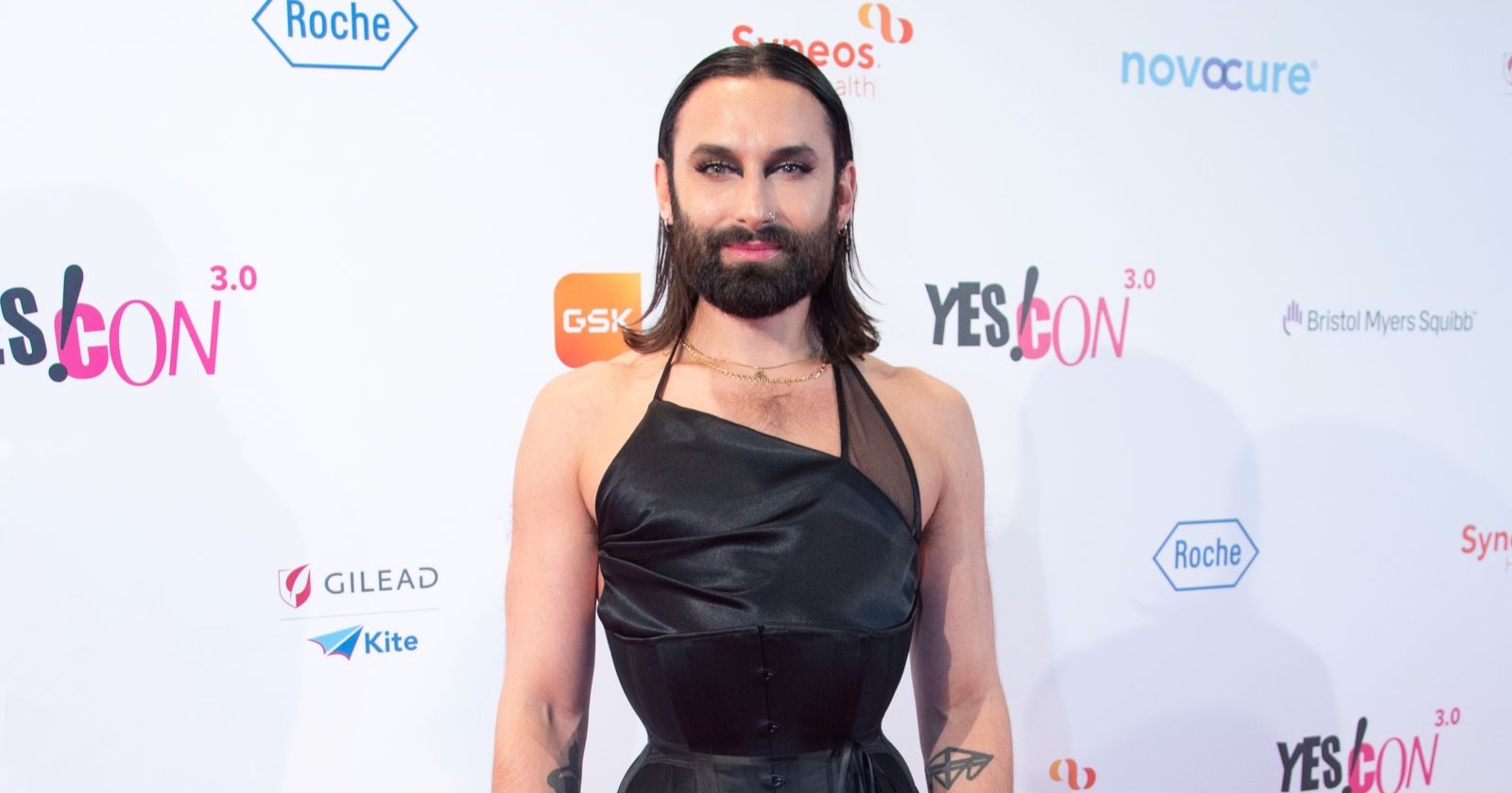 Conchita Wurst alias Tom Neuwirth posiert auf dem roten Teppich bei einem Event. Der Sänger trägt ein schwarzes Outfit und blickt in die Kamera.