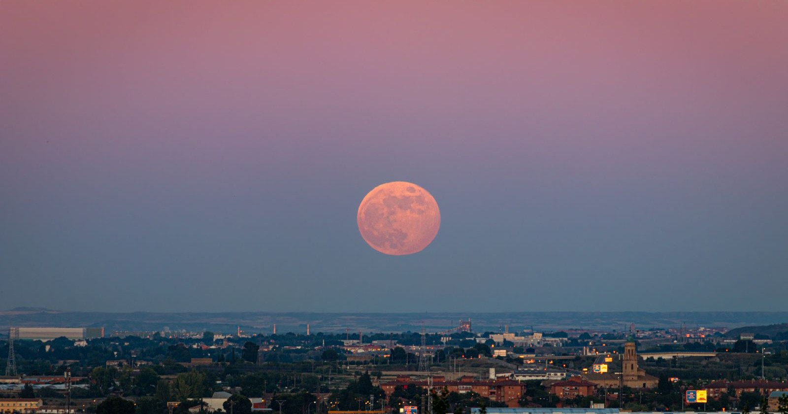 Erdbeermond 2026 als rötlicher Vollmond tief über dem Horizont bei Sonnenuntergang