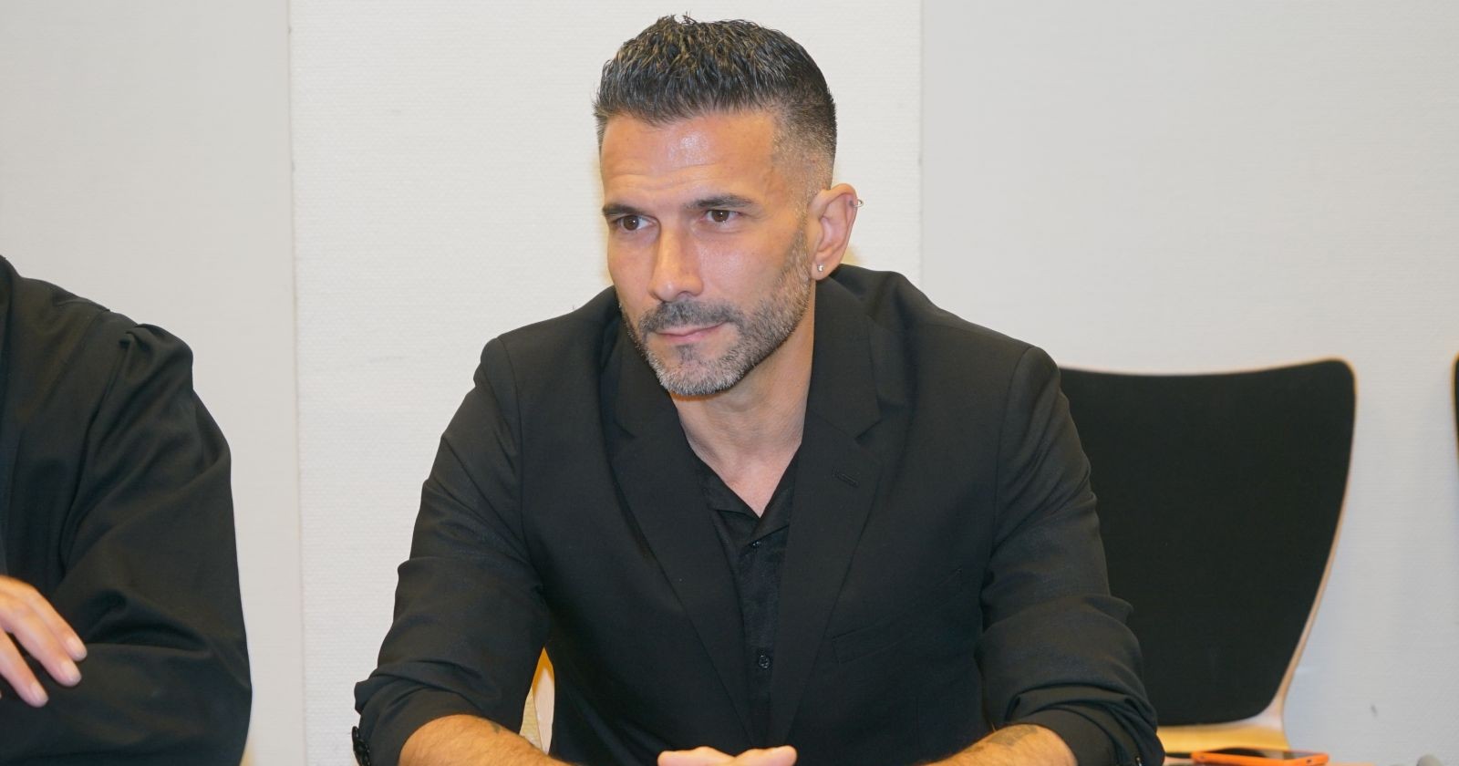Marc Terenzi sitzt bei einer Veranstaltung in einem schwarzen Anzug an einem Tisch und blickt konzentriert nach vorne.