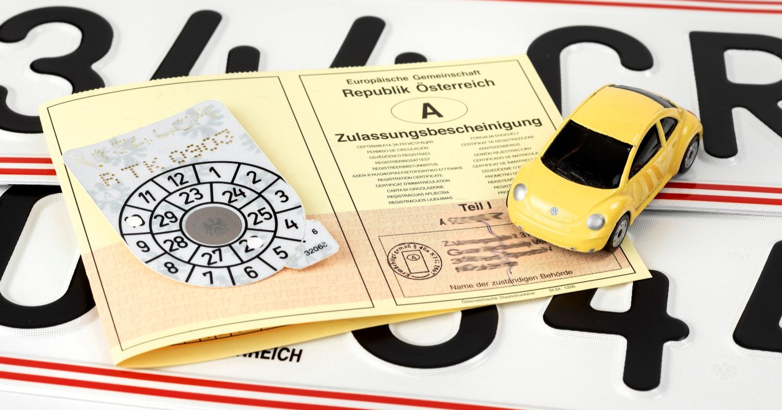 Zulassungsschein, ein Pickerl sowie ein Miniaturauto sind zu sehen