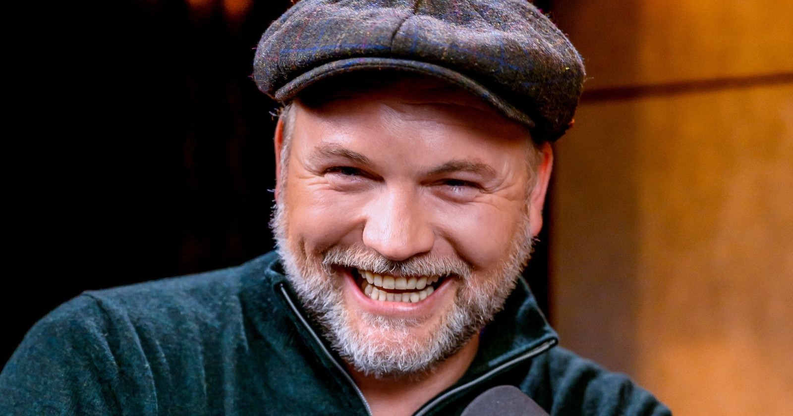 Thomas Stipsits lächelt bei einem öffentlichen Auftritt in die Kamera und trägt eine dunkle Schiebermütze sowie einen Bart./ Thomas Stipsits wird für seinen neuen Kinofilm „Italien oder Non mio Esolo“ zum Schlagerstar
