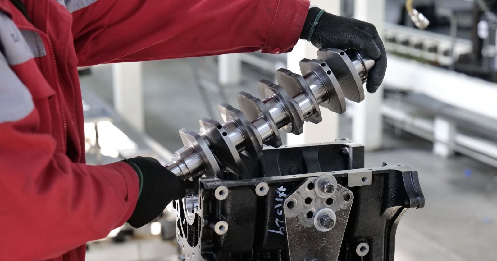 Mitarbeiter montiert eine Kurbelwelle in einem Motorblock in einem Volkswagen-Werk – Symbolbild für Stellenabbau, Konzernumbau und die Transformation der Automobilindustrie.