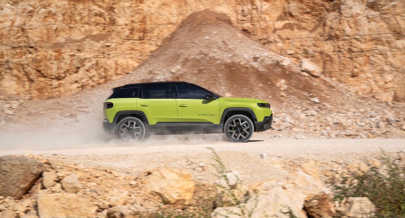 Ein zitronengelber Jeep Compass fährt auf eine staubigen Straße, vermutlich in einen Steinbruch.