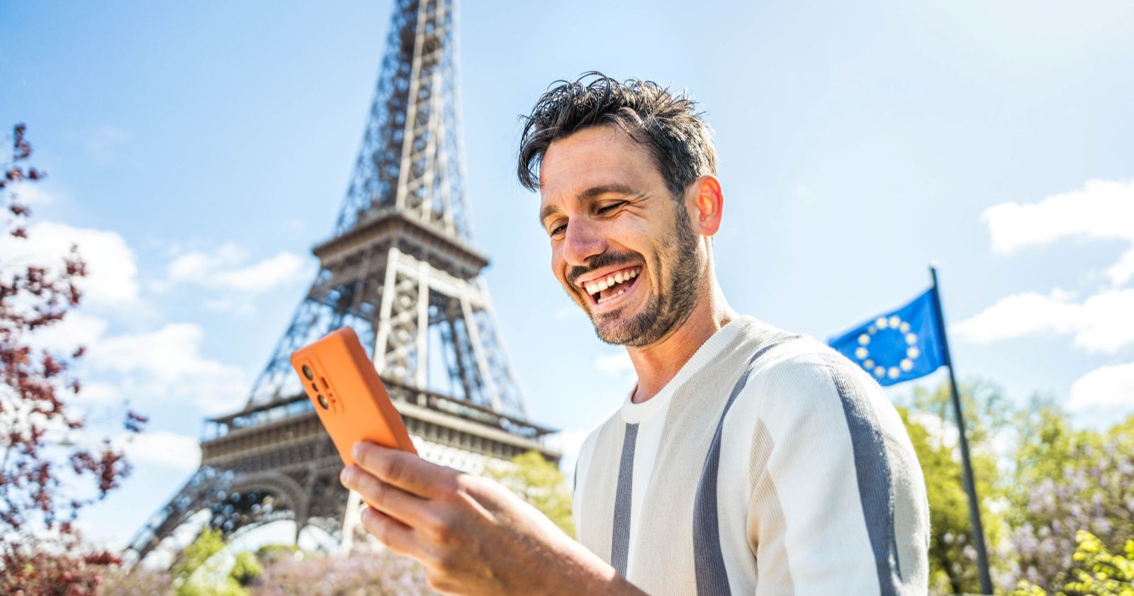 Ein Mann schaut vor dem Eiffelturm auf sein Handy.