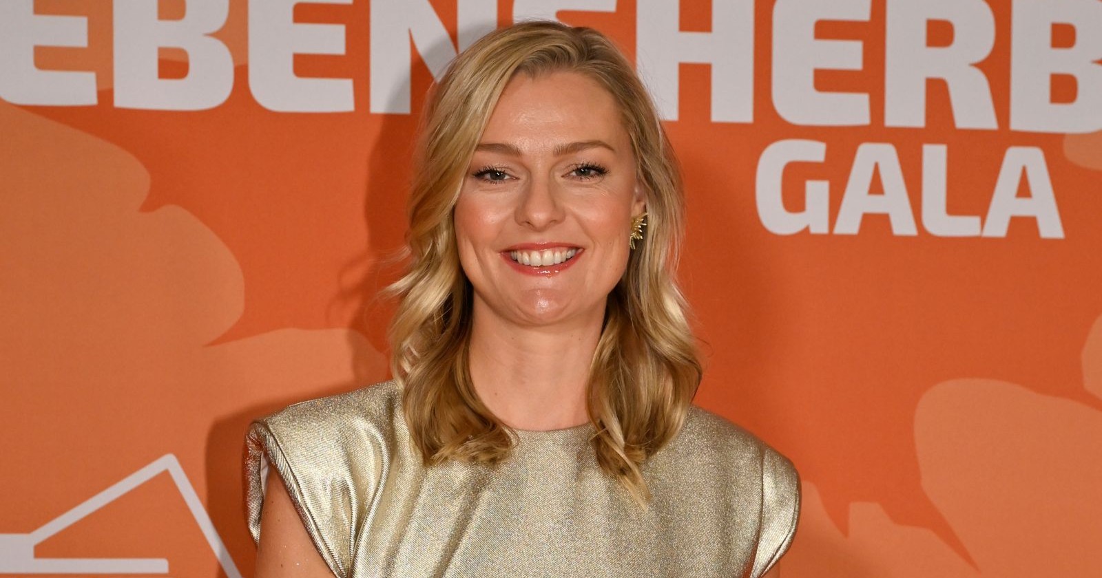 Miriam Höller lächelt bei einem öffentlichen Event in einem goldenen Kleid. Die ehemalige Stuntfrau spricht zehn Jahre nach ihrem Schicksalsjahr über Verlust, Neuanfang und ihr neues Glück.