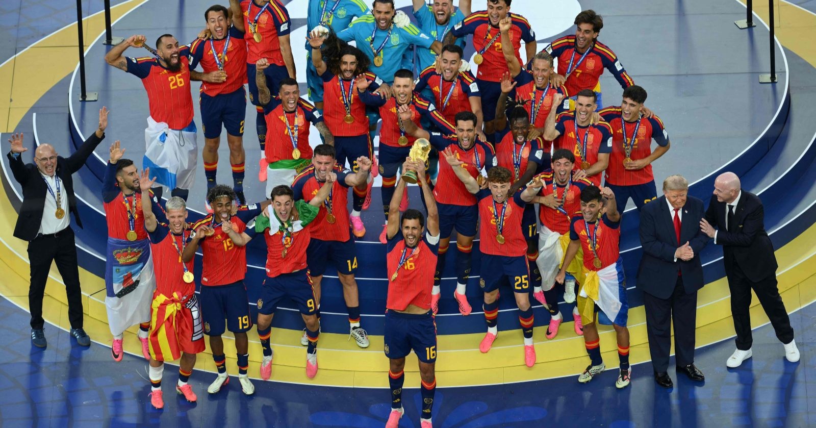 Spanien feiert den WM-Titel 2026 nach dem Finalsieg gegen Argentinien. Kapitän Rodri stemmt den WM-Pokal in die Höhe, während Donald Trump und FIFA-Präsident Gianni Infantino am Rand der Siegerbühne stehen.