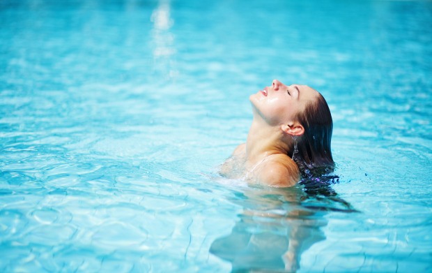 Eine junge Frau taucht mit ihren Haaren in einem Pool unter.
