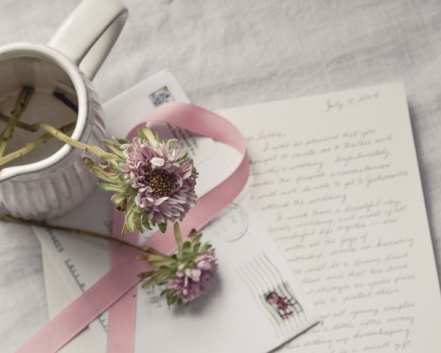 Ein handgeschriebener Brief mit einem frankierten Umschlag. Darauf Blumen, eine Vase und eine Schleife.