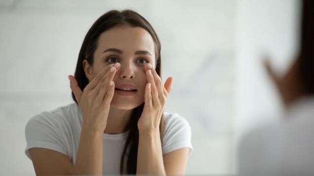 Spiegelbild einer jungen Frau, die Gesichtscreme aufträgt