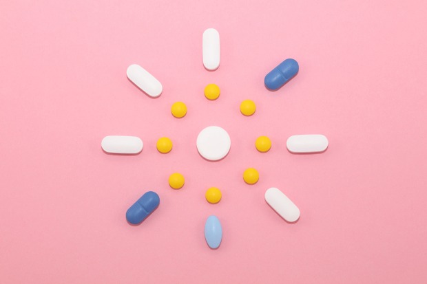 Tabletten und Kapseln wie eine Sonne auf rosa Untergrund arrangiert
