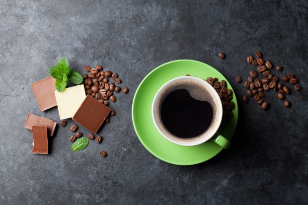Eine grüne Tasse mit schwarzem Kaffee auf einem mit mehreren kleinen Stücken Schokolade und Minzblättern dekorierten Tisch.