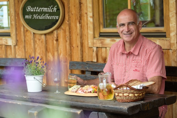 Tourismusmanager Georg Overs sitzt an einem mit einer Jause gedeckten Tisch vor einer Almhütte