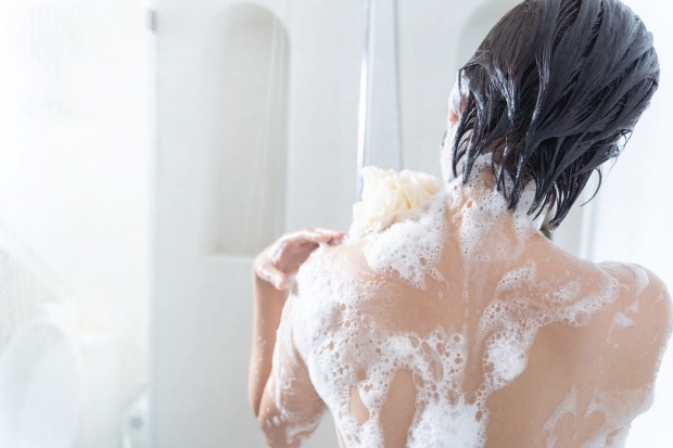 Frau von hinten in der Dusche mit eingeschäumten Rücken und Schwamm