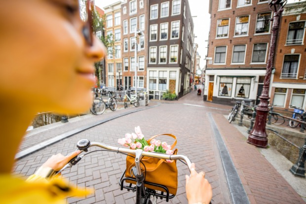 Touristin erkundet Amsterdam per Fahrrad | Credit: iStock.com/RossHelen