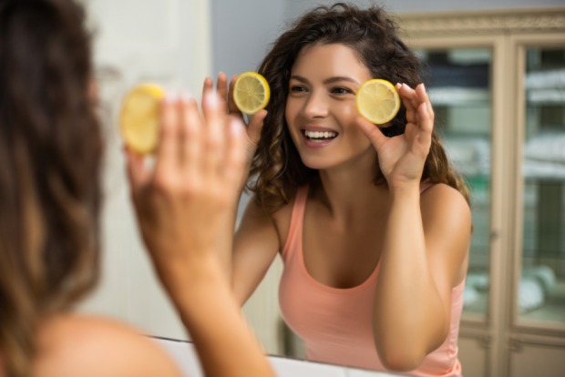 Junge Frau hält zwei Zitronenscheiben vor ihr Gesicht | Credit: iStock.com/LittleBee80
